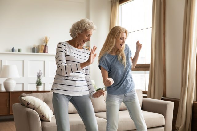 Two women dancing in front of gray couch